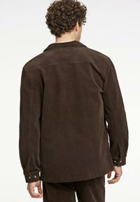 Brun kordjacka med krage, med rak skärning, långa ärmar och knappade manschetter, med en ribbad textur.