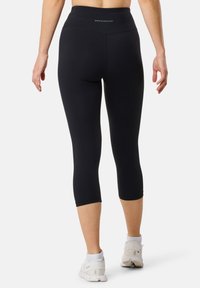 Le legging capri neri presentano una vita alta, una texture liscia e un logo sul retro. Abbinati a scarpe da ginnastica bianche.