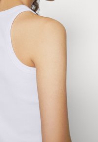 White cotton tank top featuring a rounded neckline and a sleeveless design, showcasing smooth texture and clean lines.