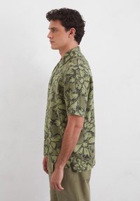 Korte mouwen shirt in olijfgroen met een zwart bloemenpatroon. Knopen aan de voorkant en een relaxte pasvorm.