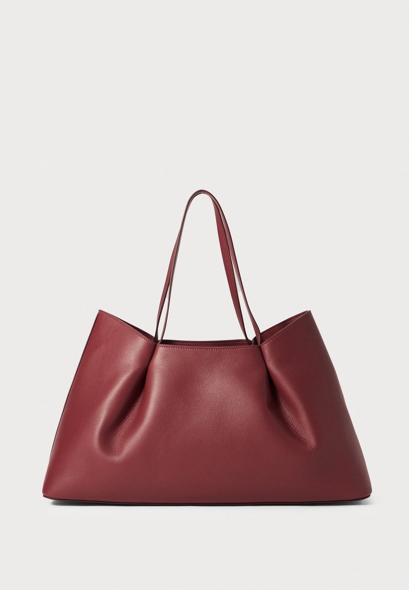 Burgundijas ādas rokassoma ar divām vidēja garuma rokturiem, ar mīkstu tekstūru, strukturētu formu un minimālistisku dizainu.