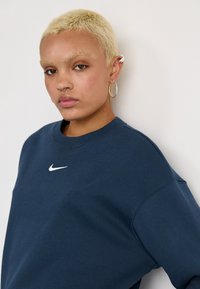 Sweatshirt azul marinho com um decote redondo e punhos canelados, apresentando um logótipo branco da Nike no peito. Tecido suave, corte descontraído.