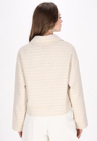 Beige ternet kort jakke med krave, lange ærmer og subtile teksturdetaljer. Har en afslappet pasform og minimale hardwareaccenter.