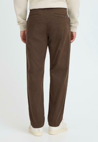 Brune bomuldsbukser med lige pasform, der har to baglommer og diskrete syninger, parret med lyse sneakers.