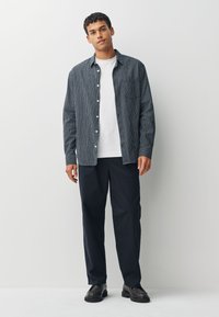 Vyriška apranga: languota tamsiai mėlyna marškiniai su baltais mygtukais, po jais dėvimas baltas marškinėlis, derinami su tamsiai mėlynomis kelnėmis ir juodais batais.