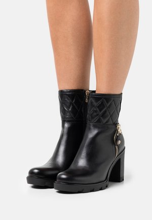 Black leather ankle boots with a quilted upper, gold zippers, and sturdy block heels, featuring a textured rubber sole for grip.