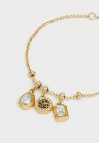 Gouden ketting met drie bedels: een druppelvormige cristal, een ronde bedel met een decoratief patroon en een rechthoekige cristal, allemaal versierd met kleine edelstenen.