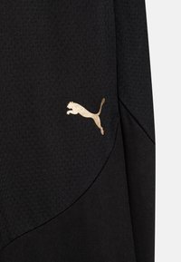 Zwarte sportieve stof met een gestructureerd patroon. Heeft een gouden Puma-logo van een springende kat aan de zijkant, waarmee het merkteken wordt benadrukt.