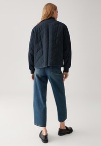 Marineblauw geborduurd jack met een staande kraag, met een gesplitst achterontwerp. Gecombineerd met een relaxte blauwe denim en zwarte veterschoenen.