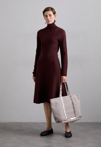 Bordová pletená šaty s dlhým rukávom a priliehavým tielkom, so sukňou do áčka, doplnené sivou taškou s kovovými pruhmi a čiernymi balerínami.