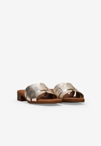 Sandalias deslizantes de oro metálico con un diseño de tiras trenzadas y un bajo tacón de bloque marrón. Textura suave y estilo de punta abierta para mayor transpirabilidad.
