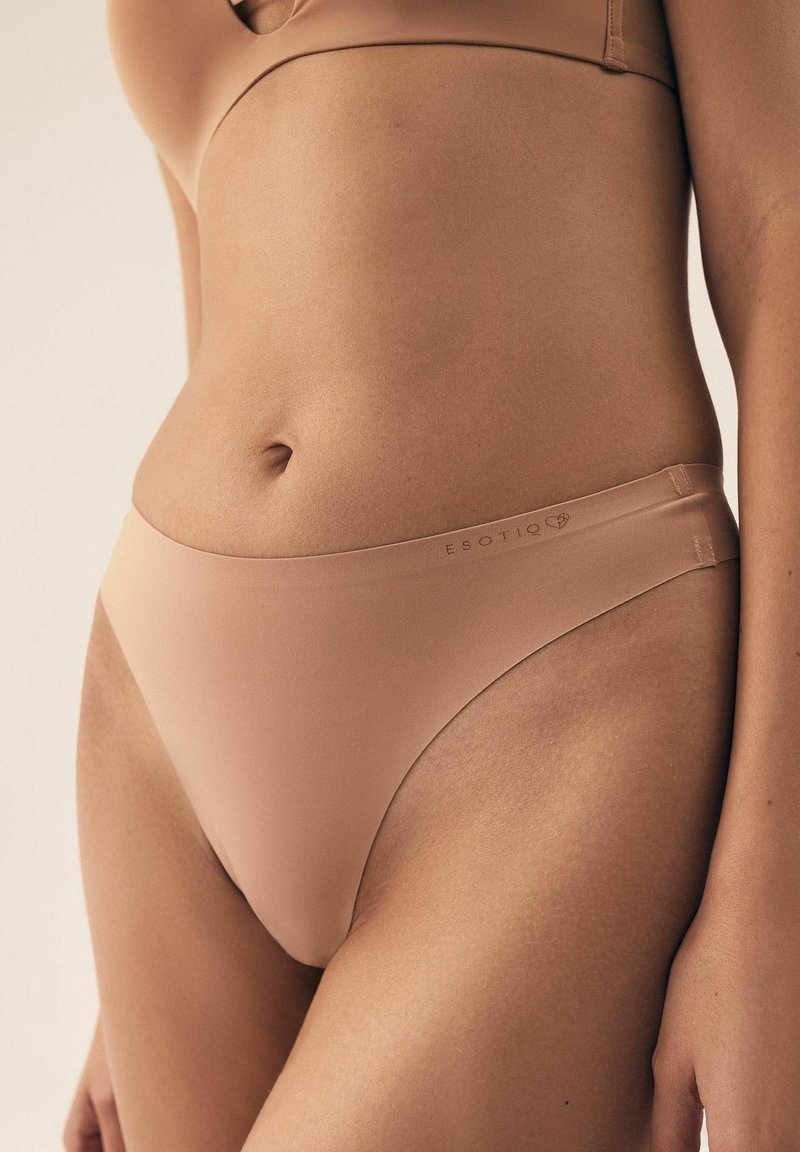 Beige Unterwäsche aus glattem, dehnbarem Stoff, mit niedriger Leibhöhe und minimaler Bedeckung, sowie dezentem Branding am Bund.