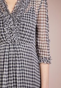 Vestido a cuadros en gris y marrón, con mangas transparentes, escote con volante y puños rizados, que presenta una textura en la tela y una silueta fluida.