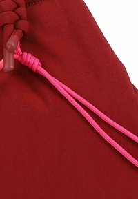Tela roja con textura suave que presenta dos cordones rosa, uno atado en un nudo y el otro enrollado, para asegurar una bolsa o funda.