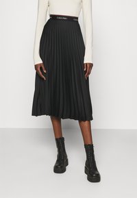 Gonna midi plissettata nera con cintura elastica di Calvin Klein. Presenta una superficie liscia ed è abbinata a stivali militari neri con lacci.