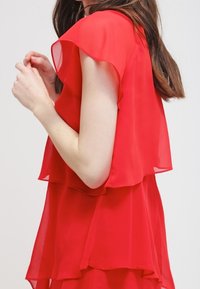 Blouse rouge à plusieurs couches avec de courtes manches volantées en tissu transparent, dotée d'une coupe ample et d'un design fluide.