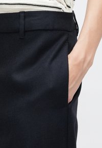 Black fabric skirt featuring a smooth texture, side pocket, and a tailored waistband. The design is simple and modern.