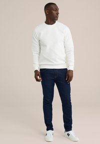 Vit texturerad sweatshirt med rund halsringning, ihop med mörkblå slim-fit jeans och vita sneakers med svarta accenter.