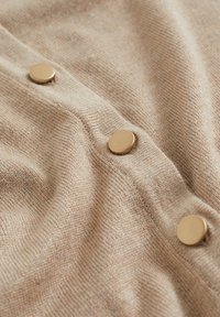 Beige stickad tyg med tre runda, släta beige knappar som är vertikalt placerade på den texturerade klädyta.