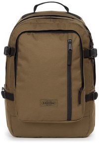 Sac à dos en tissu brun de forme rectangulaire, avec une poche zippée à l'avant, des sangles de compression sur les côtés et une poignée de transport sur le dessus.