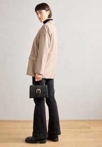 Blazer beige sopra un dolcevita nero, abbinato a jeans a campana scuri e scarpe platform nere chunky. Tiene una piccola borsa nera con hardware dorato.
