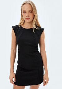 Svart åtsittande klänning med cap sleeves, slät textur och en elegant, strukturerad design. Har sömdetaljer längs framdelen.