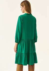 Vestido verde en capas de tejido ligero, con mangas largas y puños elásticos. Presenta un corte relajado y un escote redondo.