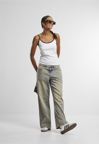 Biely tielkový top s čiernym lemovaním, svetlomodré roztrhané džínsy a biele tenisky s čiernymi pruhmi. Čierne štvorcové slnečné okuliare a náušnice.