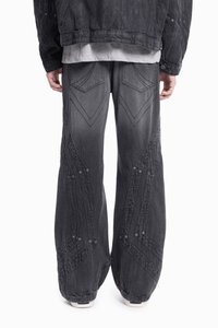 Czarne dżinsowe spodnie typu wide-leg z wyraźnym ściegiem w zygzak i guzikami, w połączeniu z teksturowaną czarną kurtką i szarym T-shirtem.