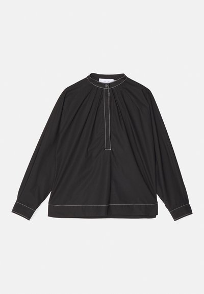 Blusa negra de manga larga en tejido ligero, con un frente fruncido, cuello abotonado y costuras blancas en contraste a lo largo del dobladillo y los puños.