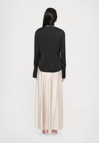 Črna bluzo z dolgimi rokavi, gladke teksture in visokim ovratnikom, v kombinaciji z dolgotrajno, svetlo rožnato satenasto krilo, vidno s hrbtne strani.