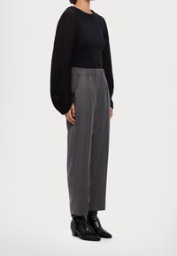 Haut noir à manches longues avec texture côtelée, associé à un pantalon gris taille haute et des bottines noires à talon légèrement brillant.