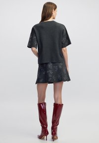 Donkergrijs gebreid topje met korte mouwen, in combinatie met een bijpassende flared rok met bloemenpatronen; aangevuld met glanzende rode kniehoge laarzen.