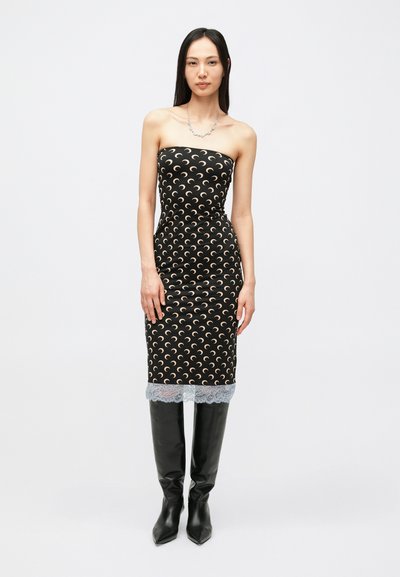 Vestito nero senza spalline con motivo a mezzaluna, design aderente, bordo in pizzo all'orlo, indossato con stivali neri al ginocchio.