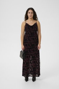 Maxi dress in dark purple lace with floral pattern, spaghetti straps, and slight sheen. Paired with a small black crocodile-textured handbag.