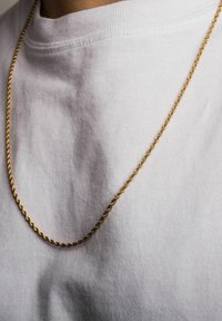 Gylden snoet kædehalssmykke hviler på en hvid t-shirt. Kæden har et snoet design, der tilføjer tekstur og glans til det samlede look.