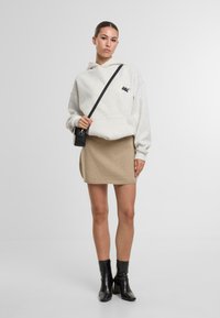 Felpa oversize grigia chiara con logo, abbinata a una mini gonna in maglia beige. Modella che indossa stivali neri alla caviglia e una piccola borsa nera. Sfondo semplice.