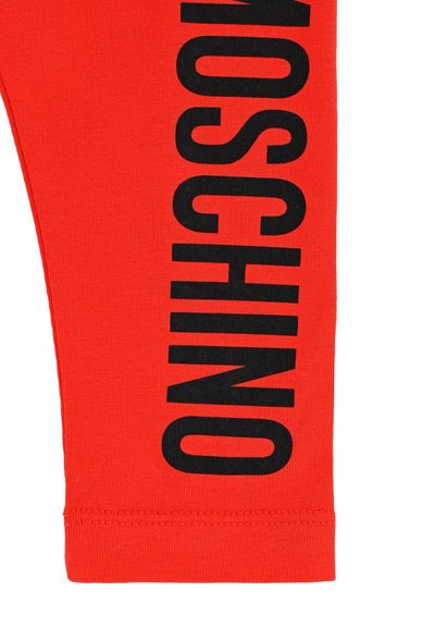 Czerwone legginsy bawełniane z wyraźnym czarnym napisem "MOSCHINO" wzdłuż boku. Gładka tekstura, dopasowany krój i starannie wykończone wykończenie.