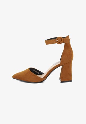 Scarpa con tacco alto in suede marrone, con punta affusolata, cinturino alla caviglia con fibbia circolare e tacco cilindrico spesso.