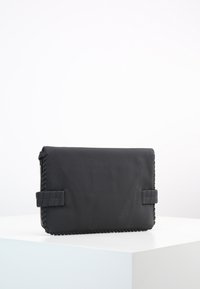 Borsa a mano in pelle nera con superficie testurizzata, caratterizzata da bordi intrecciati e un design piatto. Si chiude con dettagli in tessuto intrecciato su ciascun lato.
