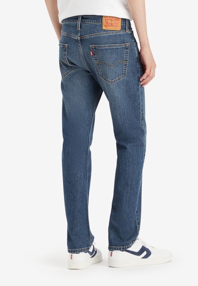 Blaue Denim-Jeans mit geradem Bein, mit einem Lederpatch auf der Rückseite und zwei Gesäßtaschen. Tragen sie mit weißen Sneakern.