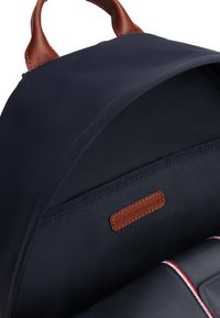 Εσωτερικό σάκου πλάτης σε μπλε ναυτικό χρώμα με υφή λείας υφασμάτινης επιφάνειας, καφέ δερμάτινη ετικέτα και αντίθετη ραφή σε κόκκινο και λευκό χρώμα.