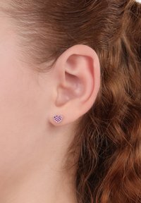 Pendientes con forma de corazón, hechos de plata, con una incrustación de piedra preciosa rosa, presentan un acabado suave y un tamaño pequeño, llevados en la oreja.