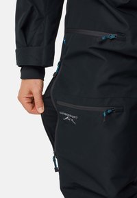 Zwarte outdoorjack met ritszakken. Kenmerken zijn onder andere een logo, gekleurde ritsaccenten en een textiel dat voor duurzaamheid zorgt.