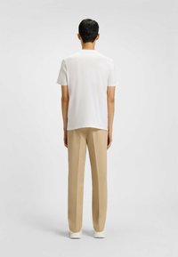 Camicia bianca a maniche corte con orlo dritto, abbinata a pantaloni beige chiaro e sneakers bianche, vista da dietro.