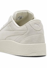 Tylny widok jasnobeżowych zamszowych sneakersów Puma, pokazujący teksturowaną platformę oraz wytłoczone logo Puma na pięcie.