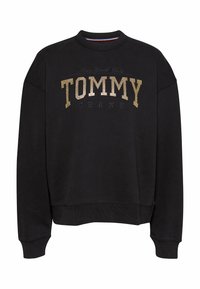 Sudadera negra hecha de tela suave, con un escote redondo y mangas largas. En la parte frontal muestra "TOMMY" en purpurina dorada con "JEANS" debajo.
