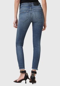 Jeans ajustados de mezclilla azul medio, con dobladillo sin rematar, bolsillos traseros de parche, combinados con sandalias negras de tiras y tacón bloque.