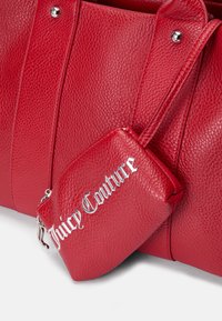 Raudona tekstūruota odinė rankinė su sidabriniais aksesuarais, turinti nuimamą mažą kišenę, pažymėtą „Juicy Couture“. Lygūs, tvirti rankenėlės.