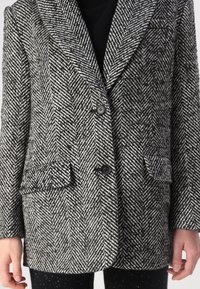 Blazer à motif pied-de-coq noir et blanc, avec un col cranté, deux boutons et deux poches avant. Le tissu texturé ajoute de la profondeur.